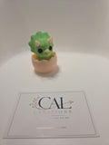 Front view of green baby triceratops clicker in beige eggshell