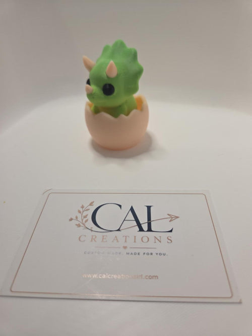 Side view of green baby triceratops clicker in beige eggshell