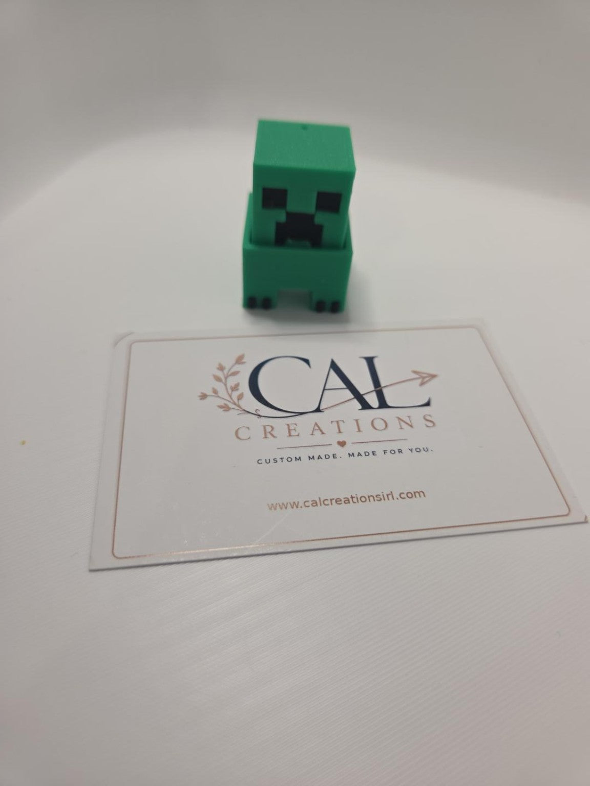 Front view of green pixel-style Creeper clicker with CalCreations branding