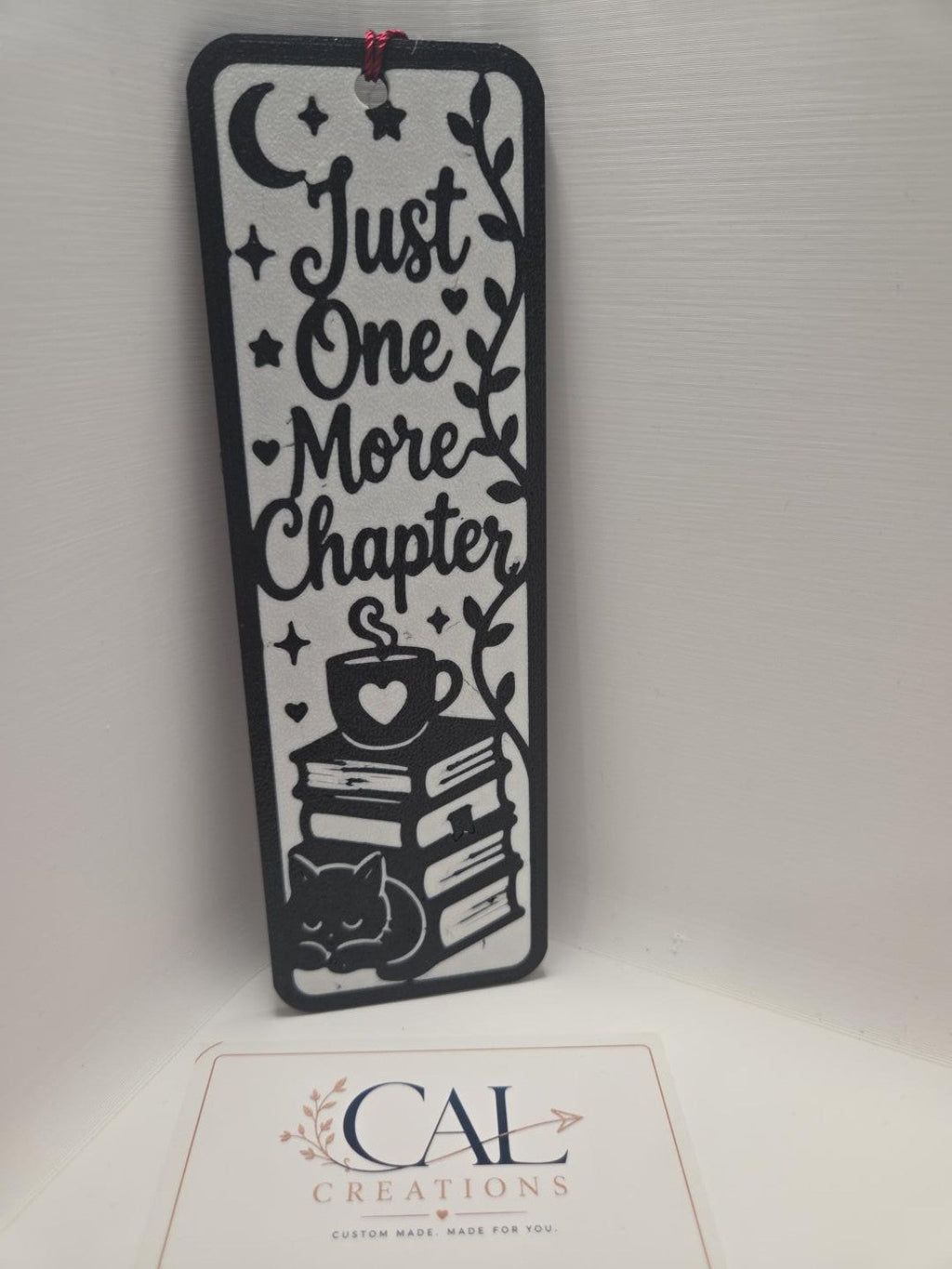 Front view of black and white Just One More Chapter bookmark with burgundy tassel