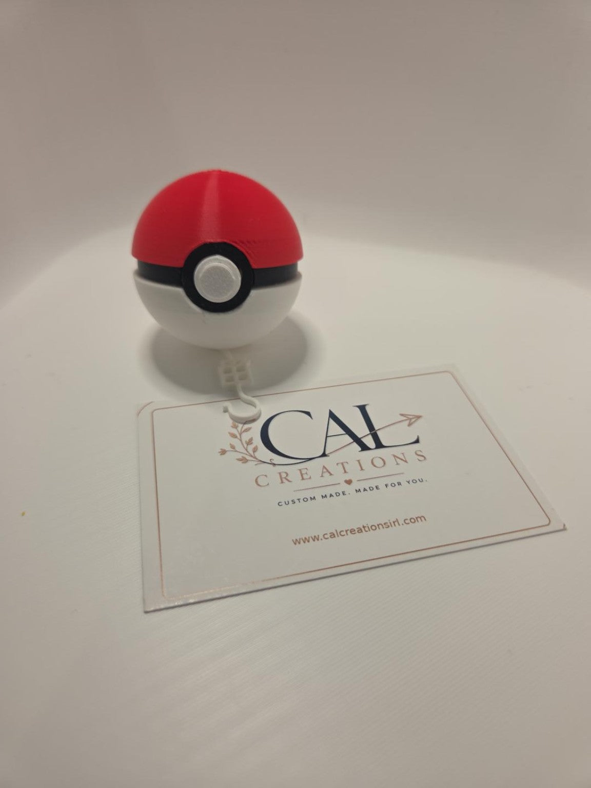 Front view of red white and black Poké Ball clicker with decorative hook visible