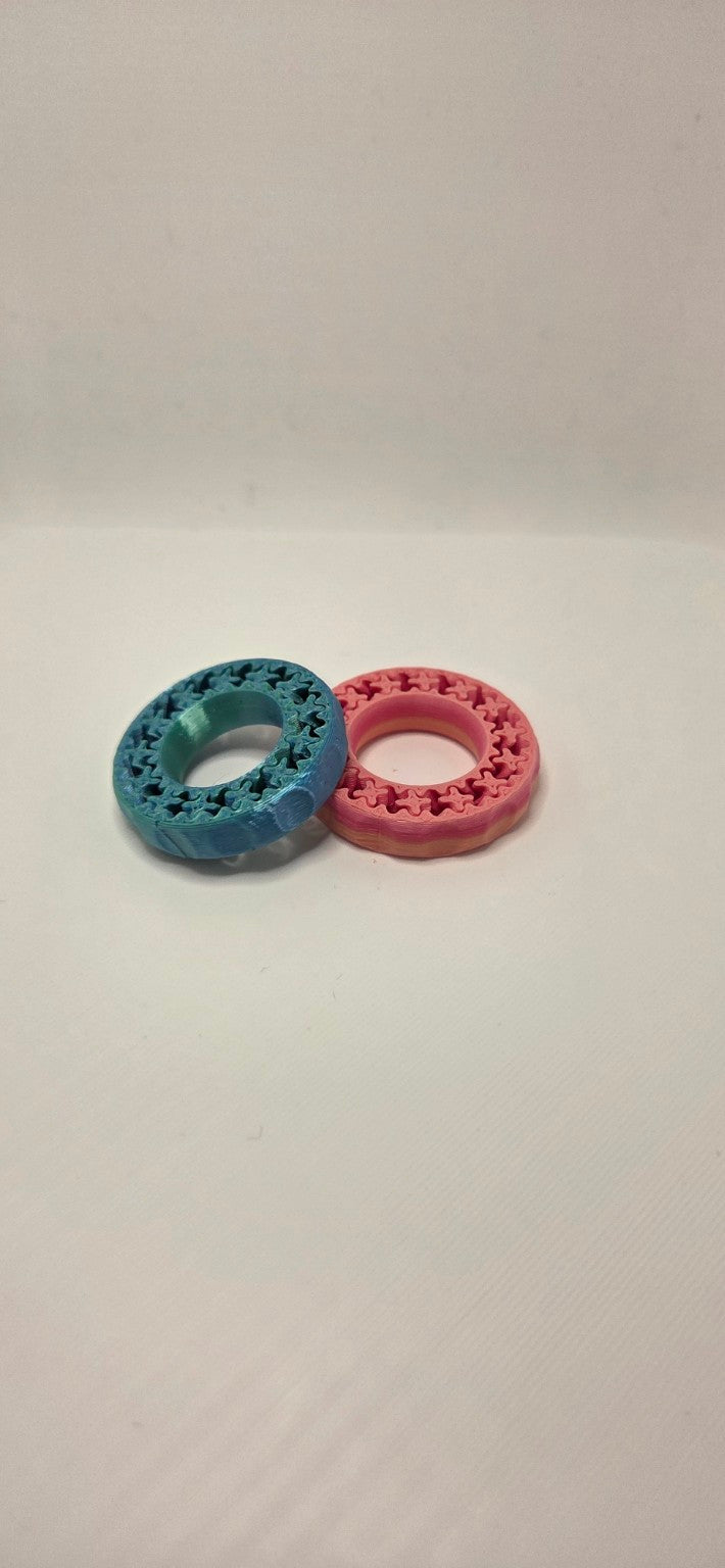 Two 3D printed gear ring fidgets in Pink Gradient and Blue/Green Metallic Silk